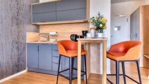 A modern kitchen with grey cabinets, a wooden countertop, and two orange bar stools.