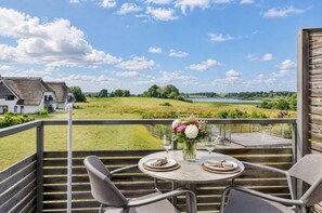 A terrace with a table set for two, overlooking a scenic landscape with a lake and rolling hills.