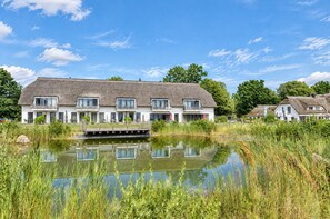A large house with a thatched roof, a small dock, and a pond in front.