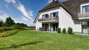 A modern two-story house with a large balcony, a well-maintained lawn, and a clear blue sky. - Vacation apartment in the Wreecher Idyll on Lake Wreechen (Putbus)