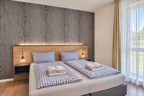 A double bed with checkered bedding, bedside tables, a wall-mounted light, and a window with curtains.