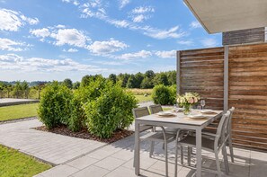 An outdoor patio with a table set for dining, surrounded by greenery and a wooden fence.