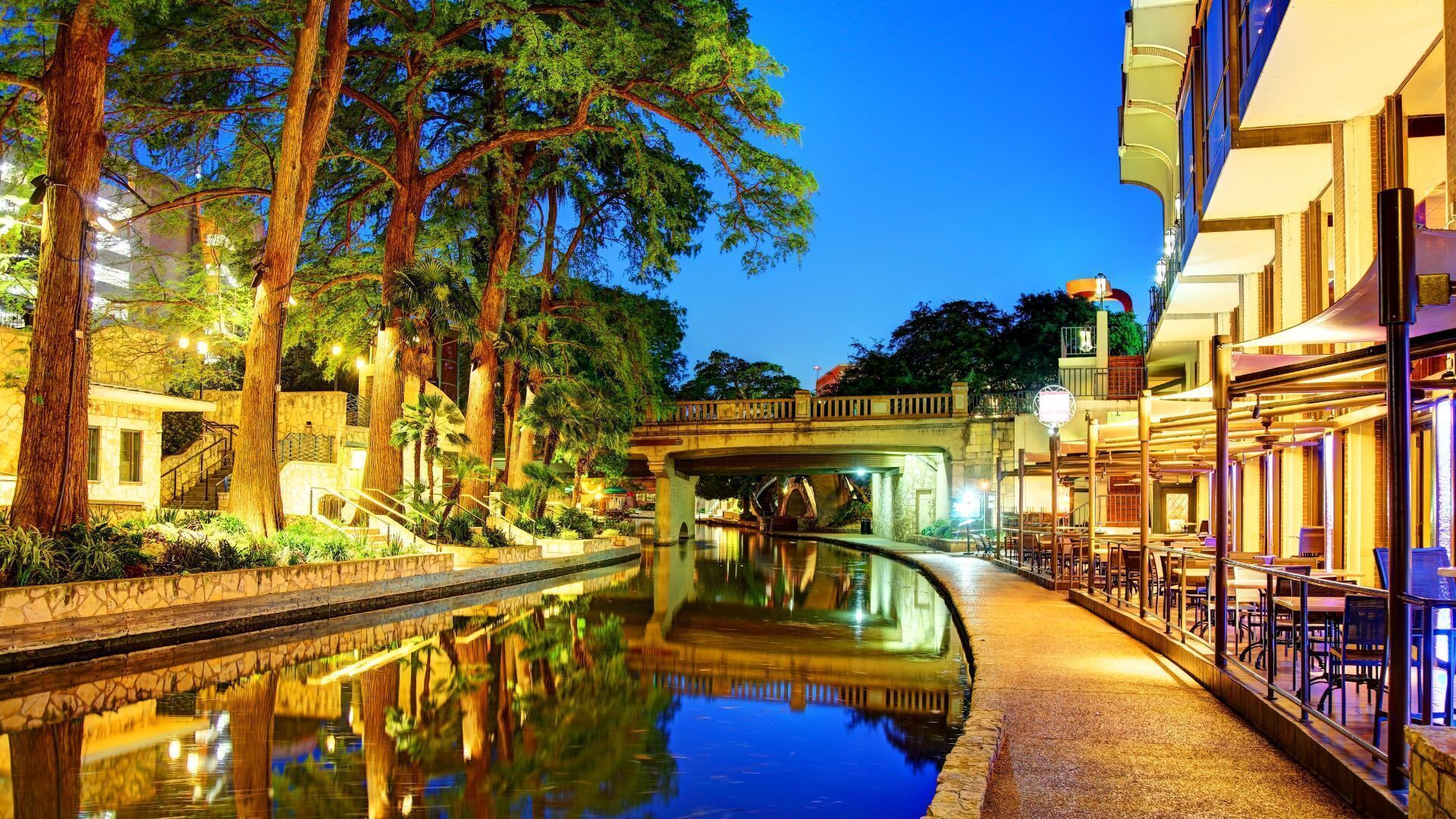 Un canal con un puente, rodeado de árboles y edificios con terrazas.