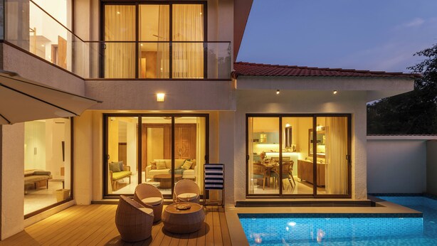 Una casa moderna de dos pisos con piscina, amplios ventanales que dan a un comedor y un balcón con mobiliario exterior.