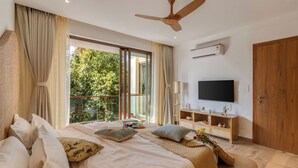 Un dormitorio con una cama grande, ventilador de techo, televisión y ventana con cortinas.