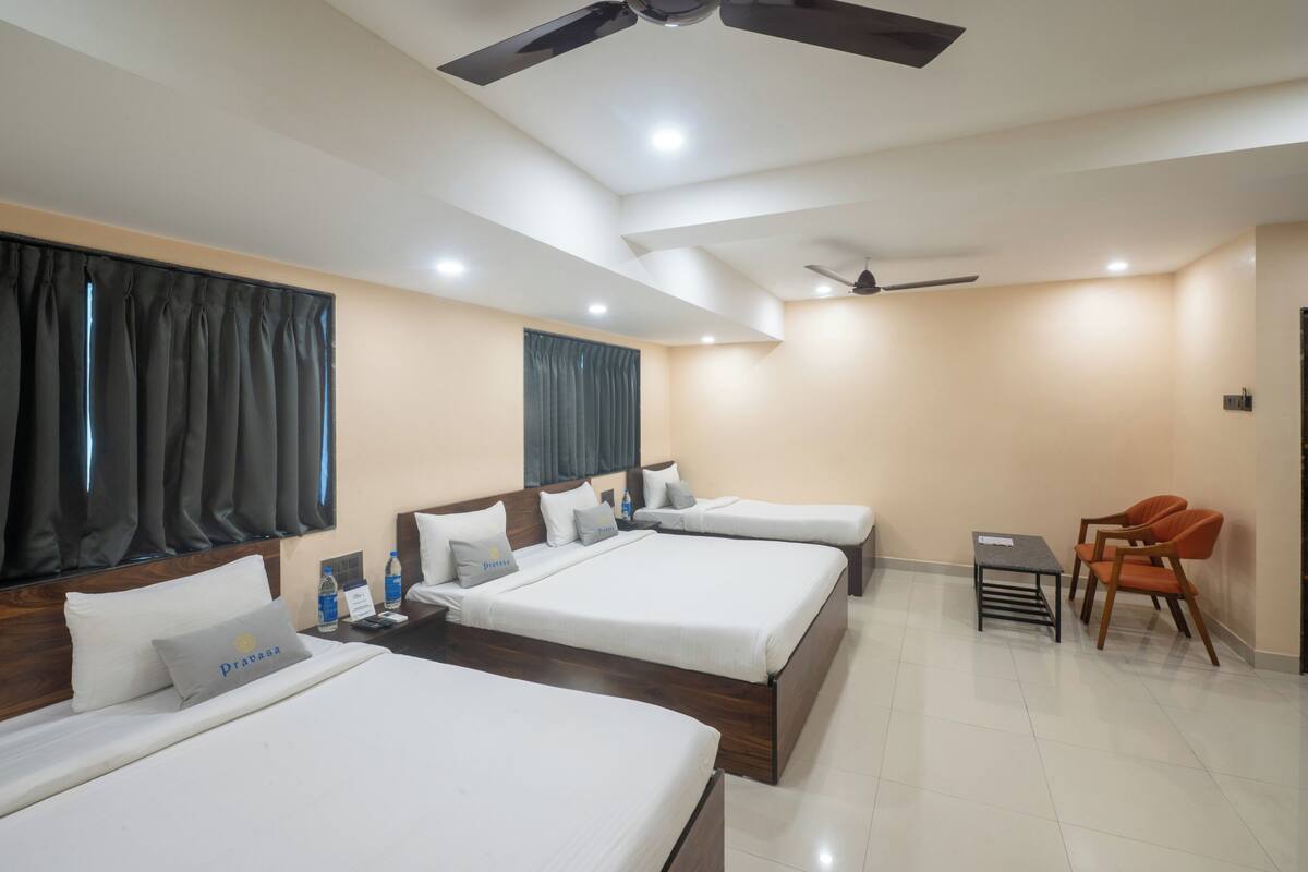 Une chambre d’hôtel avec trois lits, un bureau, des chaises et des ventilateurs de plafond.