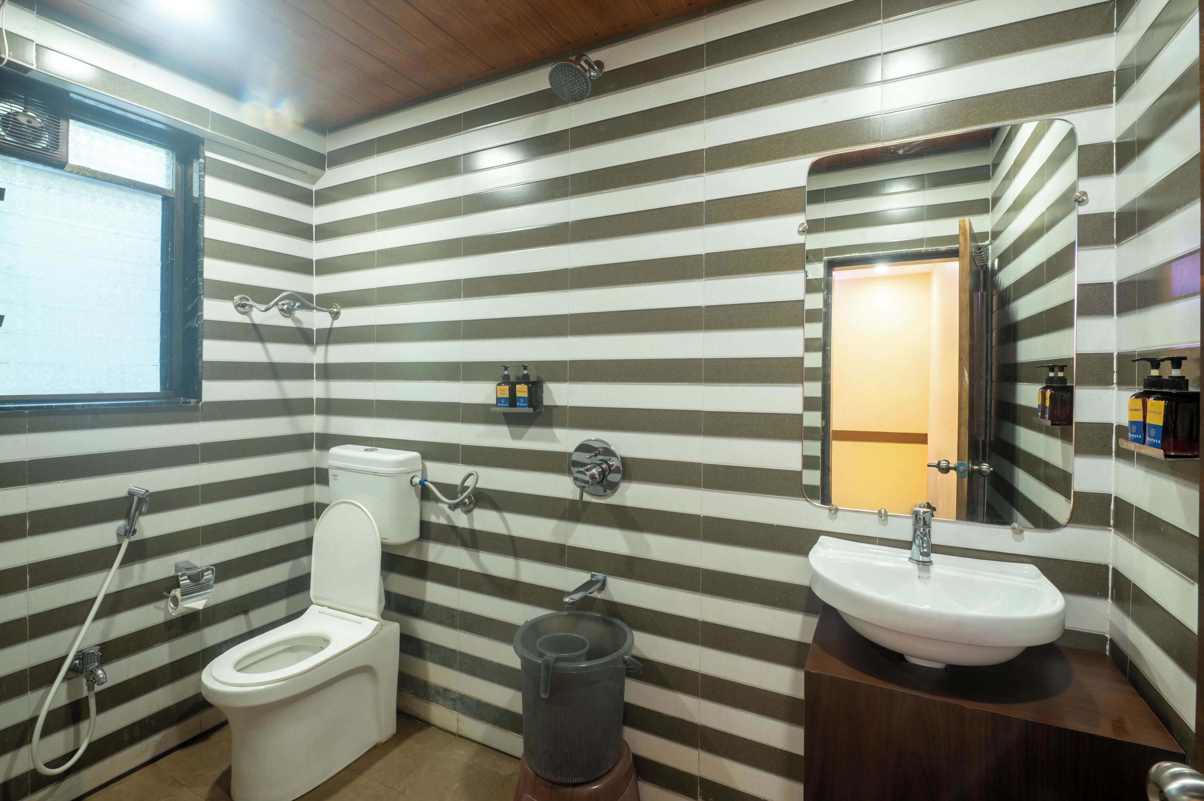 Un baño con paredes a rayas, un inodoro, un lavamanos, una ducha y un espejo.