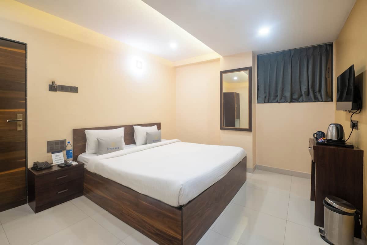 Une chambre d’hôtel avec un lit en bois, une table de chevet avec un téléphone et une bouteille, un téléviseur fixé au mur et une poubelle.