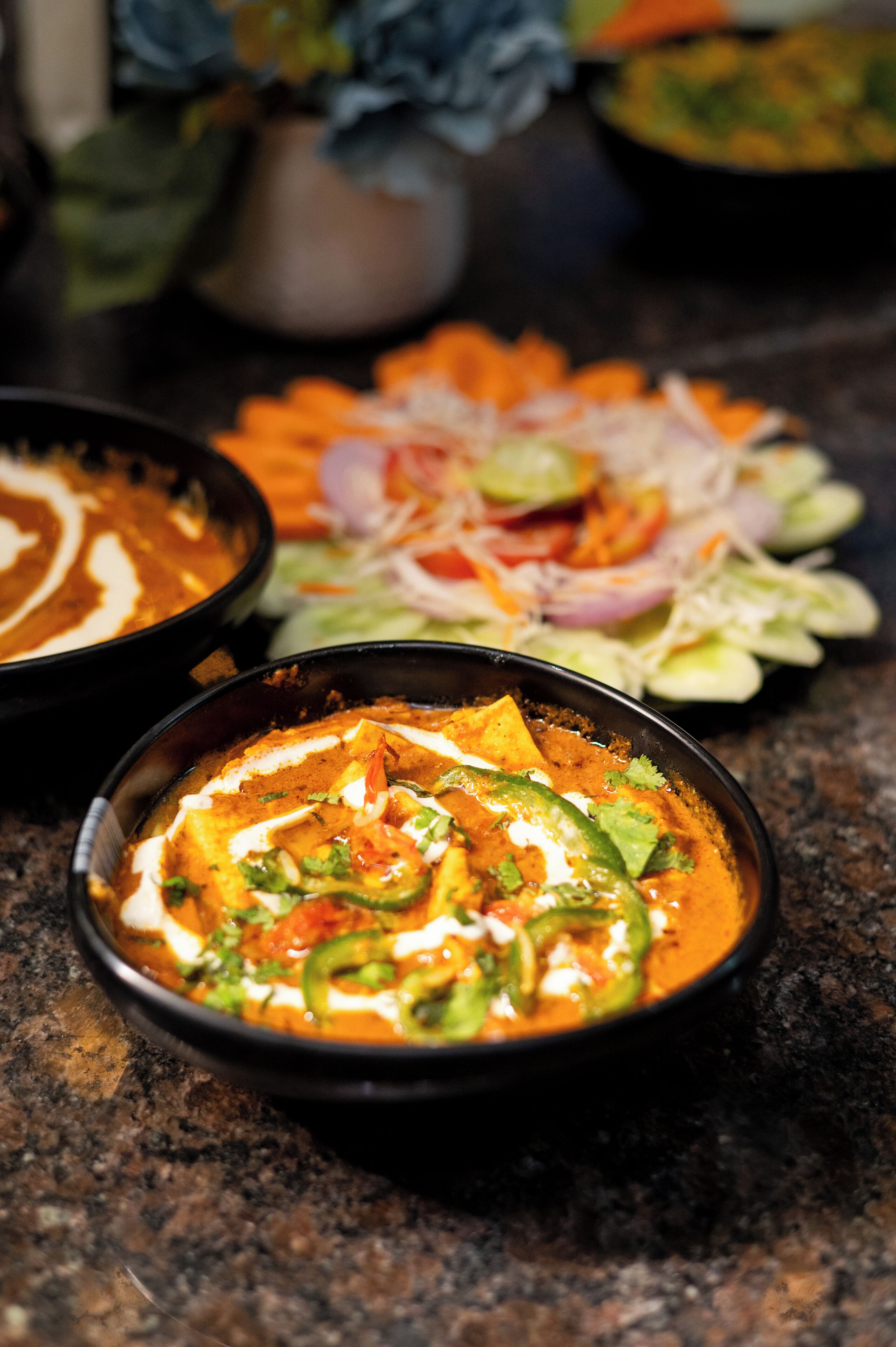 A bowl of curry with green peppers and a side salad with sliced vegetables.