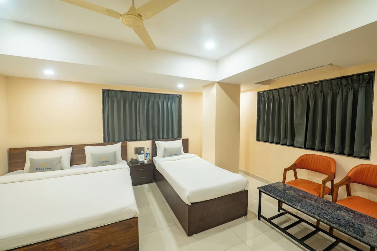 Une chambre d’hôtel avec deux lits simples, une petite table, deux chaises, un ventilateur de plafond et une fenêtre avec des rideaux.