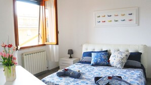 Et soveværelse med seng, sengebord, lampe, radiator, et vindue med gardiner og et billede hængt på væggen.
