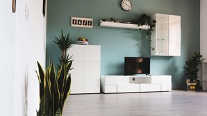 En moderne stue med et fladskærms-tv, hvide skabe, et ur og en plante.