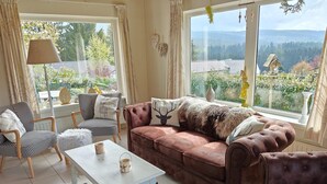 Una sala de estar acogedora con un sofá marrón, sillones estampados, una mesa blanca y un tapete de cuero de vaca.
