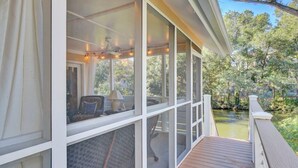 A covered deck with a view of a pond and trees, featuring a table and chairs.