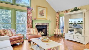 A cozy living room with striped sofas, a fireplace, a television, and a large window with curtains.