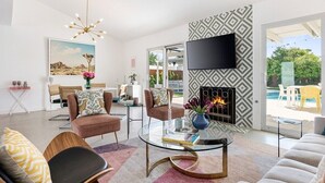 Una sala moderna con una mesa de centro de vidrio, dos sillones marrones, un sofá, una chimenea y un televisor montado en la pared.