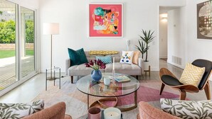 Una sala de estar moderna con una mesa de centro de vidrio, un sofá con cojines de colores y un cuadro abstracto grande en la pared.