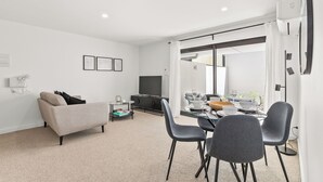 Ein modernes Wohnzimmer mit einer Couch, einem Esstisch für vier Personen und einem Fernseher.