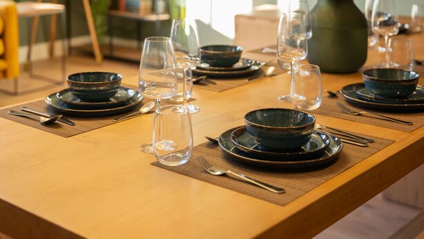 Ein Esszimmertisch, gedeckt mit Schüsseln, Weingläsern und Besteck, was auf eine festliche Tafel hindeutet.
