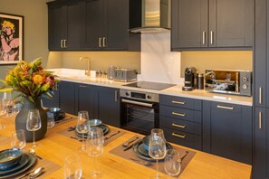 A modern kitchen with dark cabinets, a built-in oven, and a countertop with a coffee machine and toaster.