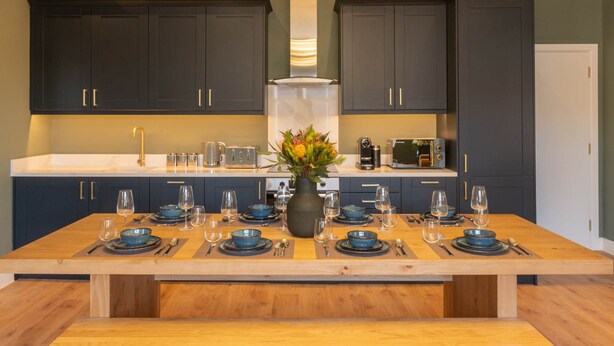 A modern kitchen with dark cabinets, a wooden dining table set for six, and a vase with flowers. - Host Stay The Georgian Quarter at Catharine House III (Liverpool)
