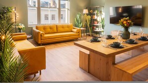 A modern living room with a yellow sofa, a wooden dining table set for six, and a bookshelf filled with books and decorative items. - Host Stay The Georgian Quarter at Catharine House III (Liverpool)