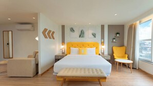 A modern hotel room with a large bed, a yellow armchair, a small table, and a view of the city. - Bloom Boutique - Dal Lake (Srinagar)