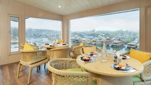A dining area with wicker furniture and a view of a water body and buildings. - Bloom Boutique - Dal Lake (Srinagar)