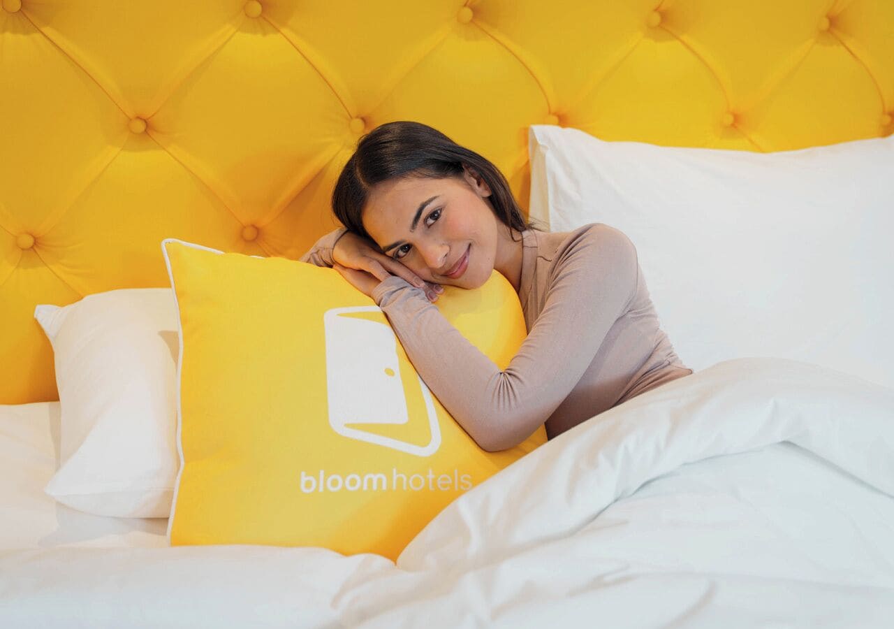 Una cama con cabecera amarilla, ropa de cama blanca y almohada amarilla con un logotipo.