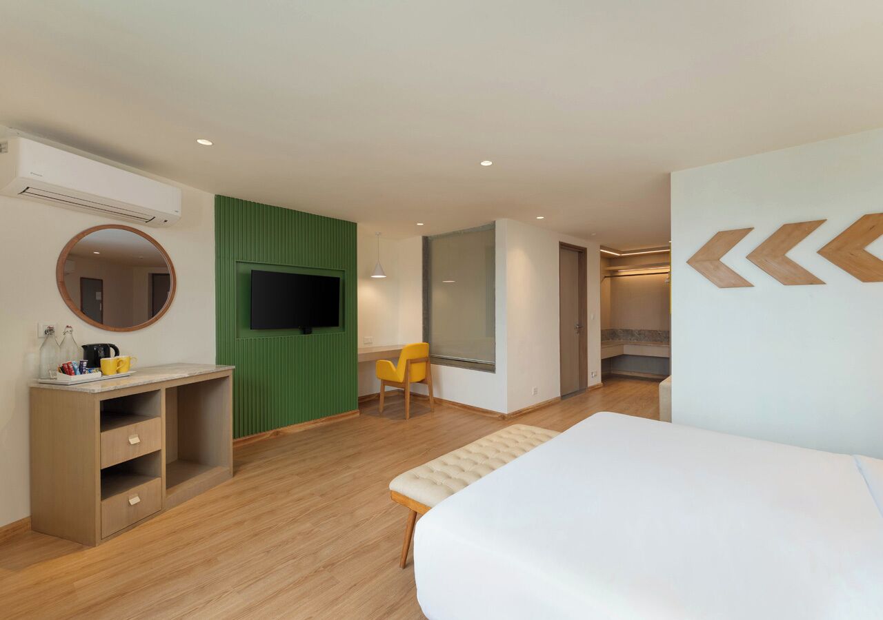 Una habitación de hotel moderna con una cama, un escritorio con cajones, una silla, un televisor y un espejo grande.