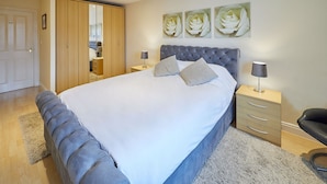 A bedroom with a large bed, a wardrobe, a nightstand, and a chair.