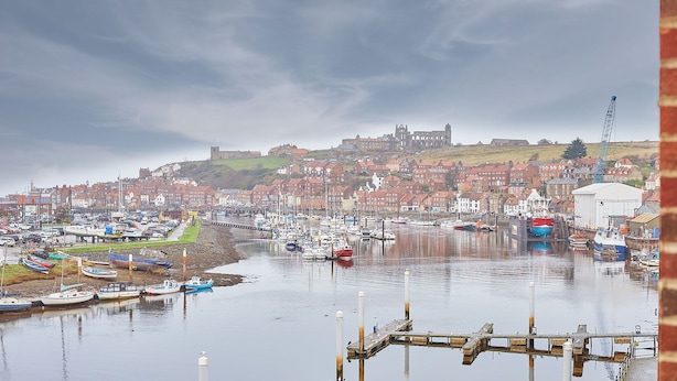 A harbor with boats, a dock, and a historic building on a hill.