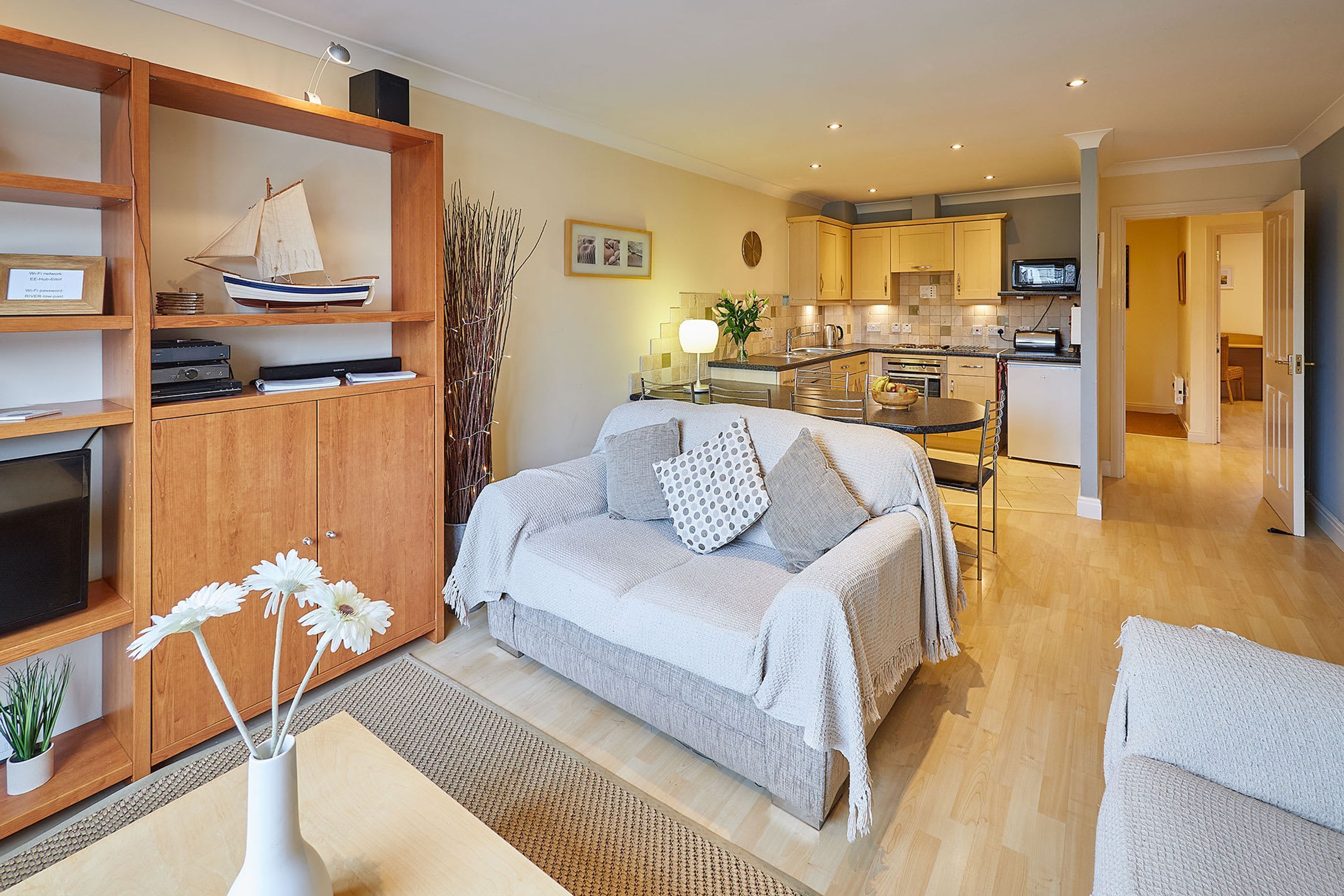 Una sala de estar moderna con un sofá, una mesa de centro y una estantería con un modelo de barco y objetos decorativos.