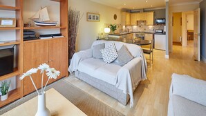A modern living room with a sofa, a coffee table, and a bookshelf containing a model ship and decorative items.