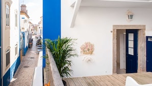 A narrow street with buildings on either side, a wooden deck, and a door with a stone frame. - Central 3 Bedroom Apartment in Ericeira (Mafra)