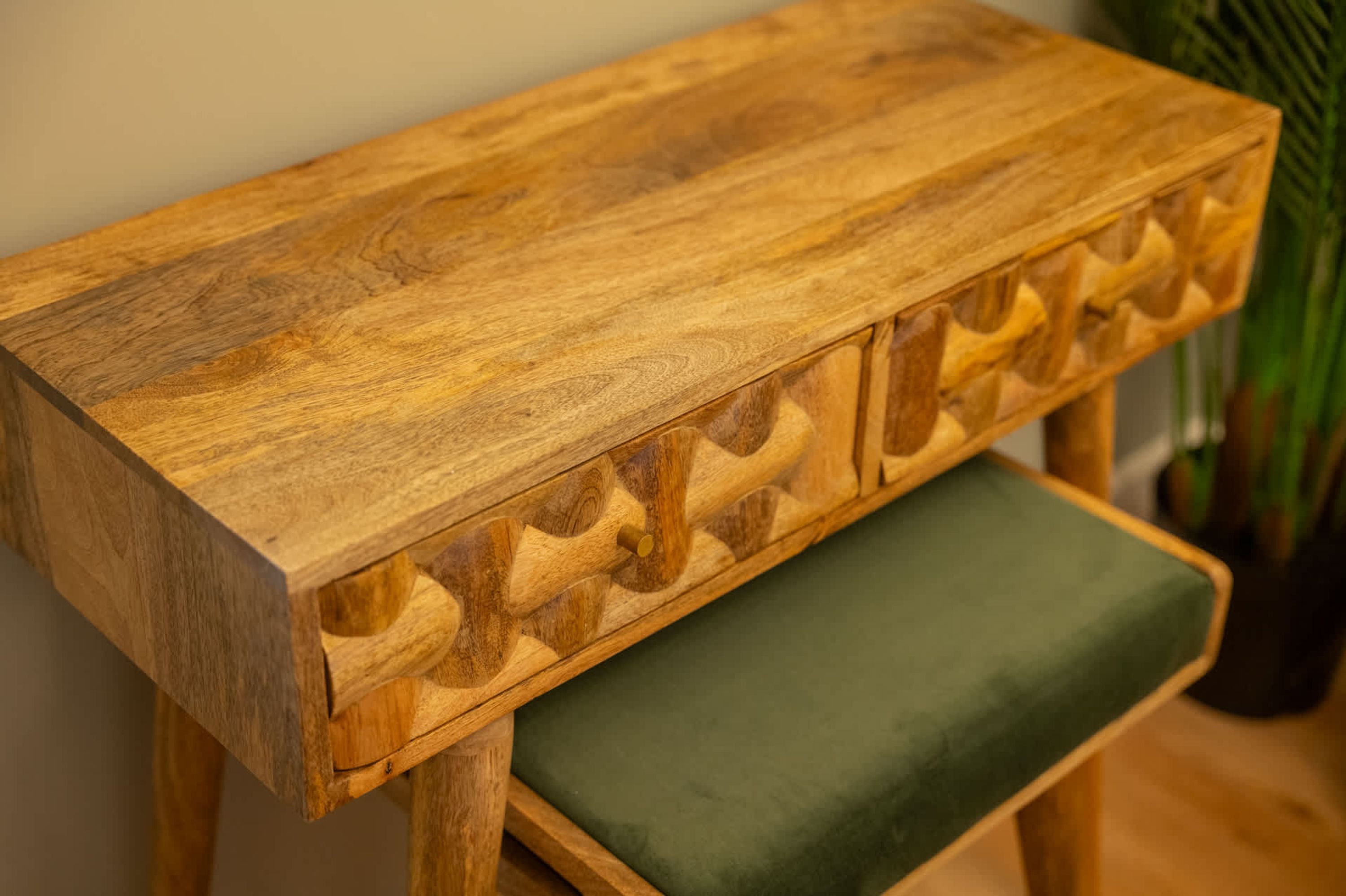 A wooden bench with intricate carvings and a green cushion.