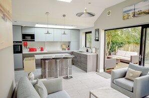 A modern kitchen with a central island, bar stools, and a dining area with a sofa and table.