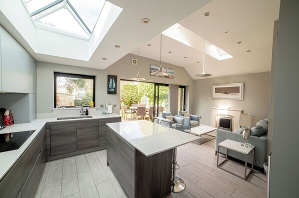 A modern kitchen with a central island, skylights, and a dining area with a sofa and table.