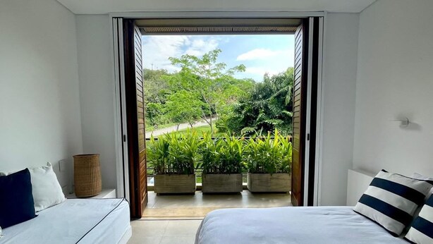 Een slaapkamer met twee bedden, uitzicht op een tuin door een geopende deur en een plafondventilator.