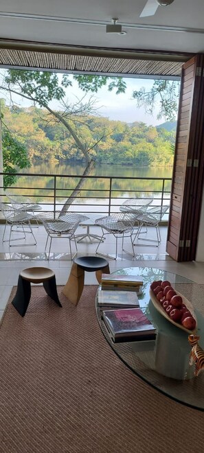 Una habitación moderna con una mesa de vidrio, dos taburetes y vistas a un lago y un bosque.
