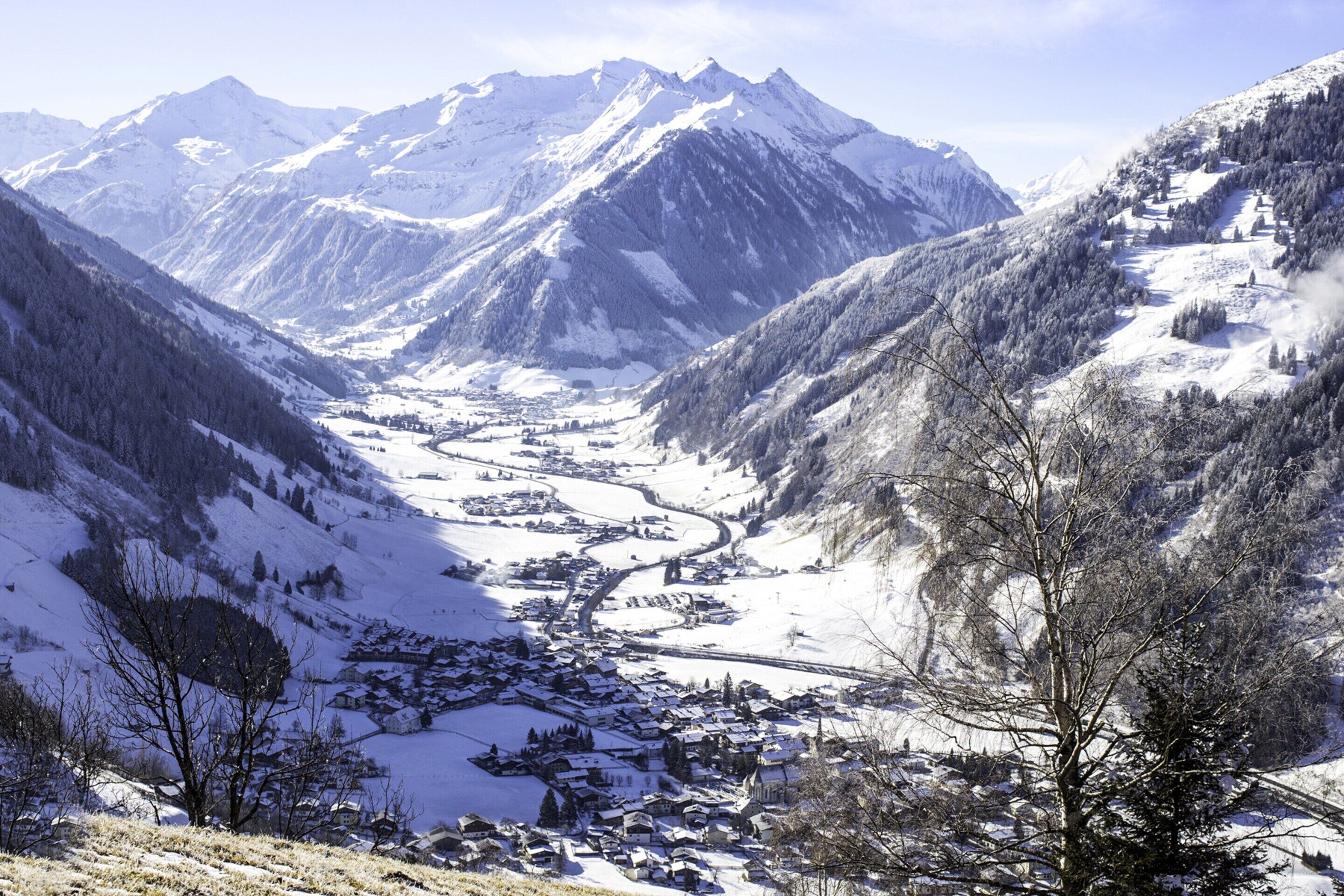 Un village de montagne enneigé, traversé par une route sinueuse qui serpente à travers la vallée, et entouré de sommets enneigés.