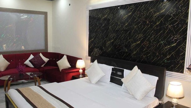 A hotel room with a large bed, a red sofa, a glass coffee table, and a large window with a black marble wall.