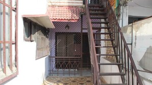 A narrow alleyway with a tiled floor, a metal staircase, and a building with a red-tiled roof and barred windows.