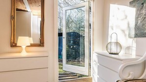 A room with a large mirror, a white chair, a small table with a lamp, and a door leading outside. - 6 Person Holiday Home in Nibe (Nibe)