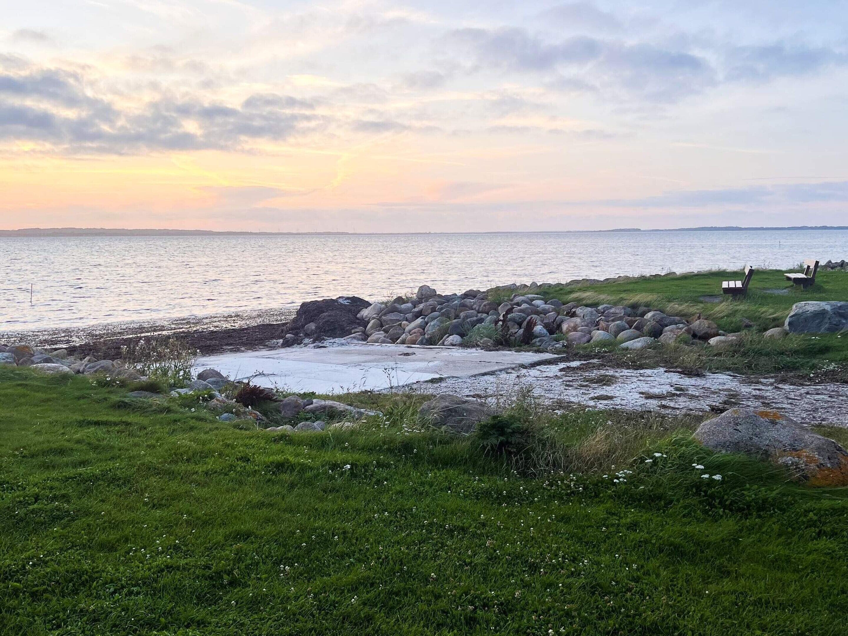 A coastal landscape with a rocky shoreline, grassy areas, and a few beach chairs.