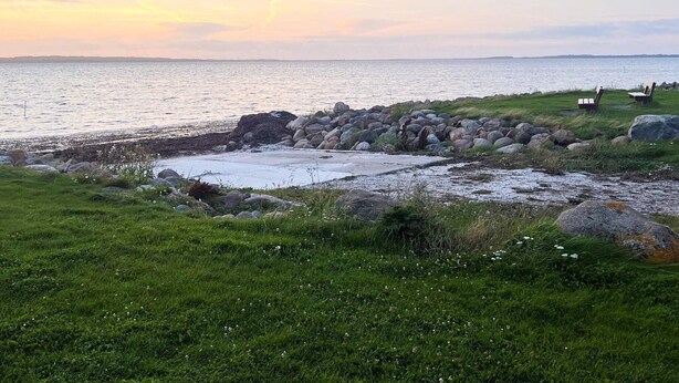 A coastal landscape with a rocky shoreline, grassy areas, and a few beach chairs. - 6 Person Holiday Home in Nibe (Nibe)
