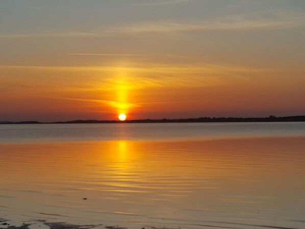 A sunset over a calm body of water with a distant shoreline.