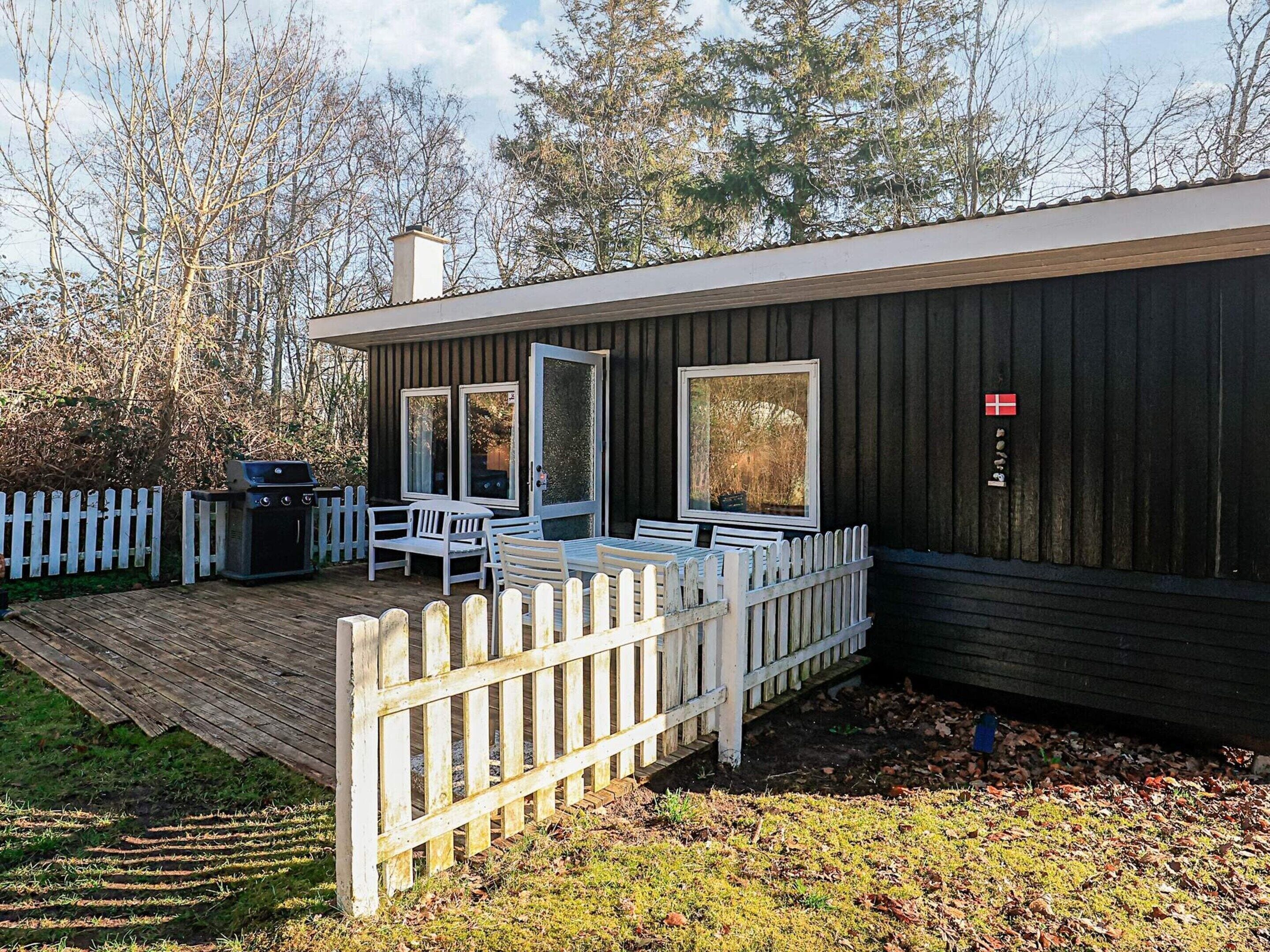 A wooden cabin with a deck, a grill, and a flag.