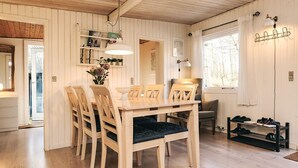 A dining area with a wooden table and chairs, a vase with flowers, and a window with a view of trees. - 6 Person Holiday Home in Nibe (Nibe)