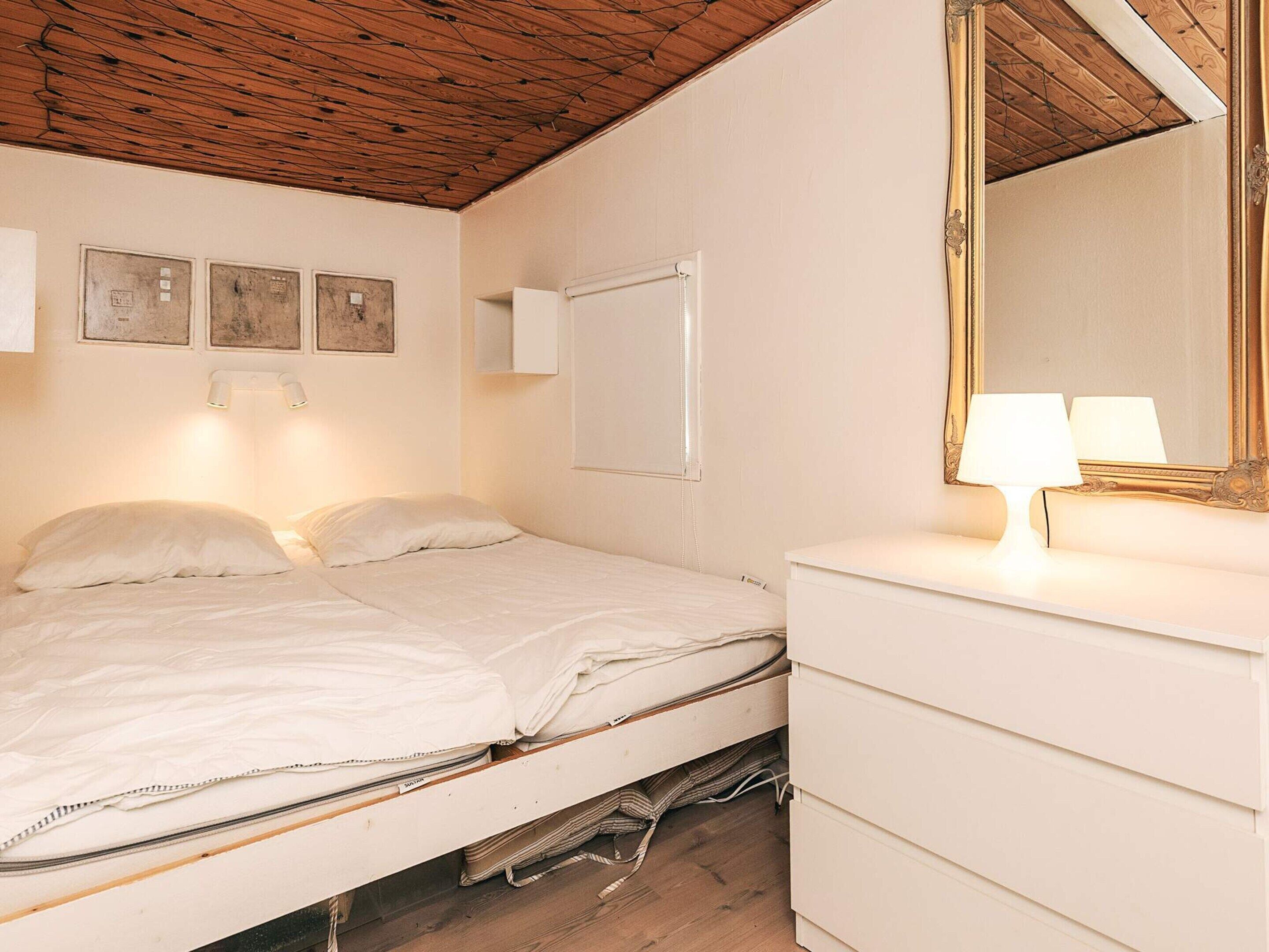 A single bed with a wooden headboard, a bedside table with a lamp, and a mirror on the wall.